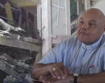 Mons. Louis Ku00e9breau, Arzobispo de Cap-Haitien (al fondo los restos del seminario de Puerto Pru00edncipe)