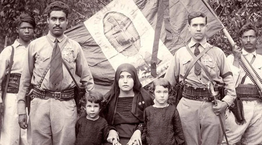 Cristeros junto a familiares, con la bandera de México detrás con la imagen de la Virgen de Guadalupe como escudo. Foto: Dominio público.?w=200&h=150