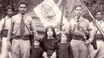 Cristeros junto a familiares, con la bandera de México detrás con la imagen de la Virgen de Guadalupe como escudo. Foto: Dominio público.