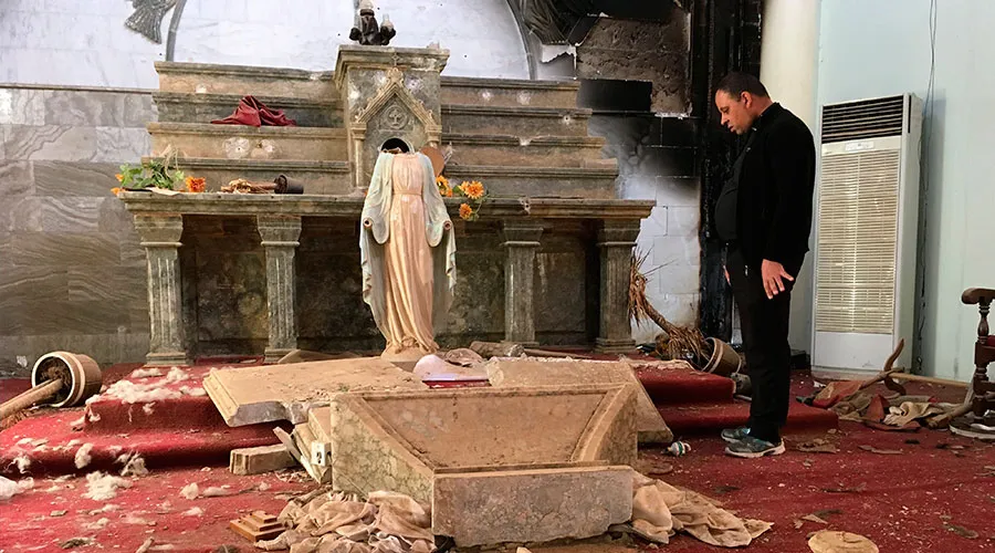 Sacerdote mira una imagen de la Virgen María decapitada, entre los escombros de una iglesia destruida por el Estado Islámico en Irak. Foto: Caballeros de Colón.