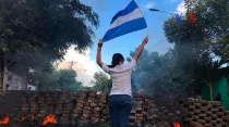 Joven sostiene la bandera de Nicaragua en medio de protestas y represión policial. Foto: Voice of America / Dominio público.