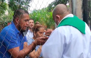 El P. Sebastiu00e1n Lu00f3pez distribuye la Eucaristu00eda detru00e1s de una malla, vigilado por la policu00eda de Nicaragua. Cru00e9dito: Diu00f3cesis Media - Radio Stereo Santa Lucu00eda 