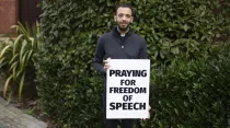 P. Sean Gough con su letrero que dice "rezo por la libertad de expresión". Crédito: ADF International