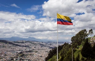Bandera de la República del Ecuador, en un día soleado con la ciudad de Quito al fondo. Crédito: Shutterstock