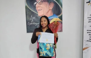 Gabby es la representante de madres del programa de Ecuador en el comité de selección de propuestas del Fondo de Innovación. De pie ante una foto del difunto cofundador de Unbound, Bob Hentzen, sostiene con orgullo el certificado de reconocimiento que Unbound le otorgó por su participación y valiosas contribuciones en el proceso de selección. Crédito: Cortesía de Unbound.