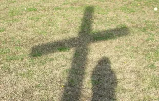Sombra de un chico y una cruz proyectadas sobre la hierba. Imagen referencial. Crédito: Pixabay.