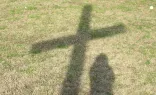 Sombra de un chico y una cruz proyectadas sobre la hierba. Imagen referencial.