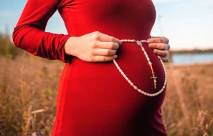 Una mujer embarazada sostiene un Rosario sobre su vientre. Crédito: Nina Hill / Unsplash