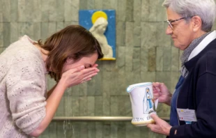 Una peregrina realiza el "gesto del agua" en las piscinas del Santuario de Lourdes. Crédito: HNDL.