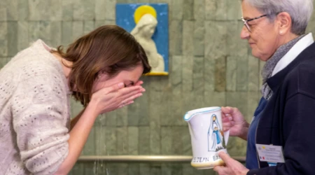 Una peregrina realiza el "gesto del agua" en las piscinas del Santuario de Lourdes.