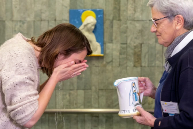 Una peregrina realiza el "gesto del agua" en las piscinas del Santuario de Lourdes.
