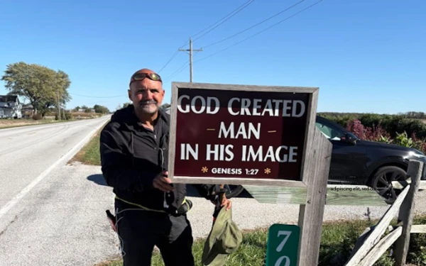 El P. Gay Graf en su travesía con una letrero que dice: "Dios creó al hombre a su imagen". Crédito: Gary Graf.