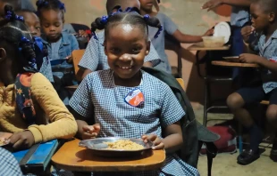 Niña haitiana sonríe ante su plato con comida, gracias a Mary's Meals Crédito: Mary's Meals