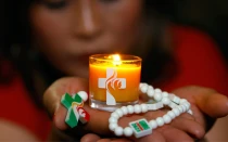 Joven sostiene una vela y un rosario con imágenes de la Jornada Mundial de la Juventud (JMJ) Lisboa 2023.