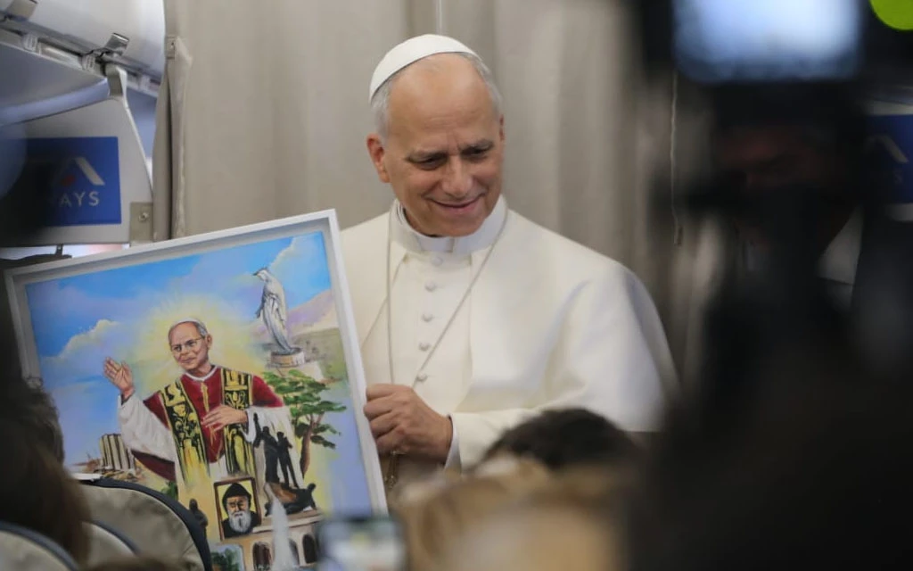 En el avión papal, León XIV muestra una pintura en la que lo han retratado. | Crédito: Elías Turk / EWTN News.