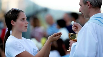 Una fiel recibe la Eucaristía de manos de un sacerdote.