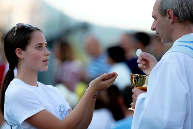 Una fiel recibe la Eucaristía de manos de un sacerdote.
