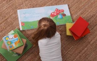 Niña de preescolar leyendo un libro en la guardería Shutterstock