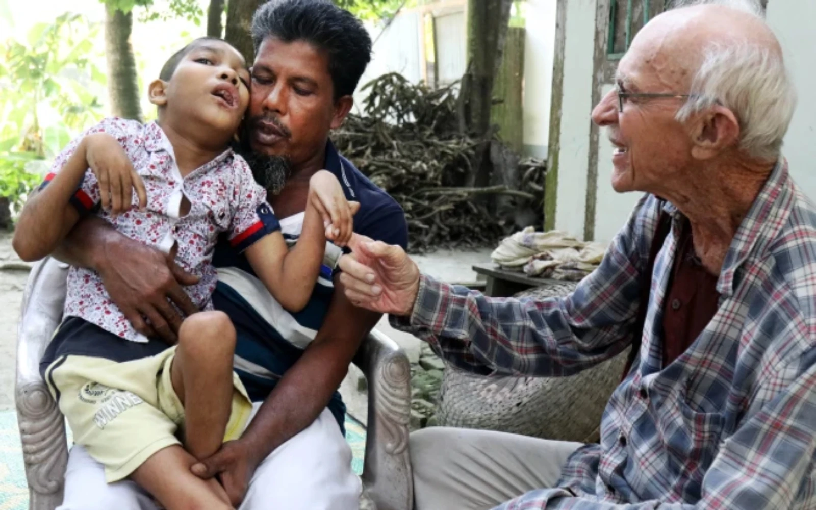 Abdul Mannan Khan y su hijo discapacitado, Abu Mosa Khan, se reúnen con el P. Robert Terence McCahill en su hogar en el distrito de Munshigonj, Bangladesh, el 18 de noviembre de 2025. El sacerdote visita aldeas a diario para encontrar niños discapacitados y conectarlos con tratamiento médico.?w=200&h=150