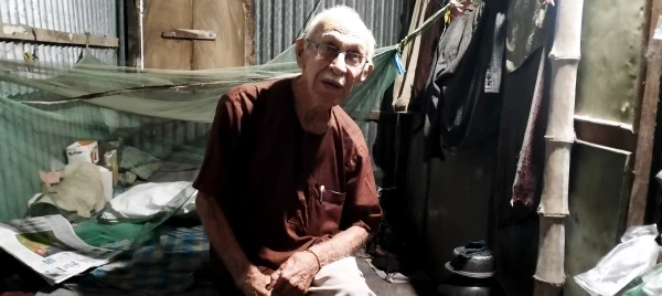 La sencilla vivienda del padre Robert Terence McCahill en un edificio escolar de Srinagar, distrito de Munshigonj, Bangladesh, mostrada el 18 de noviembre de 2025. El espacio de 1,5 x 2,4 metros, cedido gratuitamente por las autoridades locales, contiene una cama de madera, un mosquitero, una estufa de queroseno y una bicicleta. Crédito: Stephan Uttom Rozario