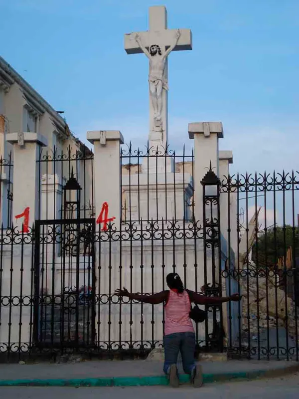 Una mujer en oración ante la Cruz aún en pie de la Catedral de Puerto Príncipe. Crédito: ACN.