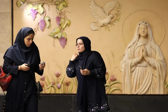 Mujeres iraníes caminan frente a un relieve de la Virgen María